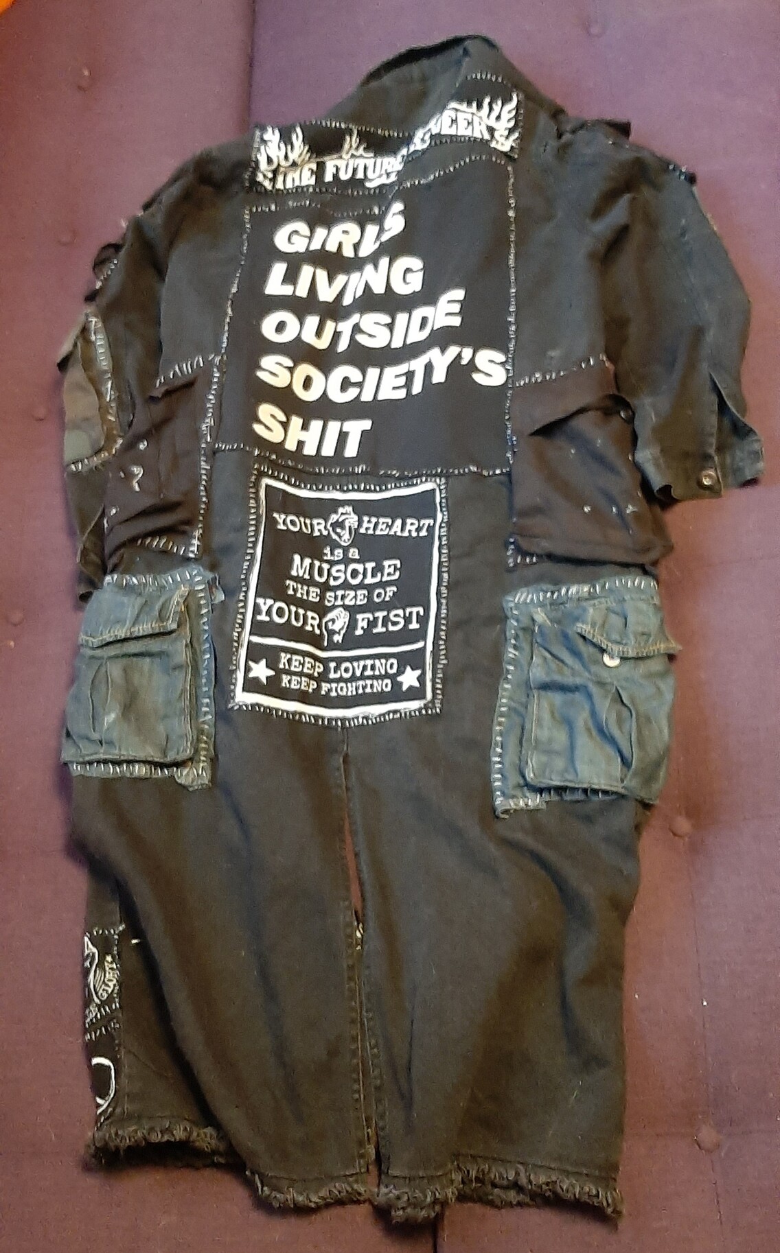 my black denim women's punk trenchcoat covered in various patches and pins and pockets. there's a shitload of fresh cargo ones sewn on the sides and shoulders. back side
