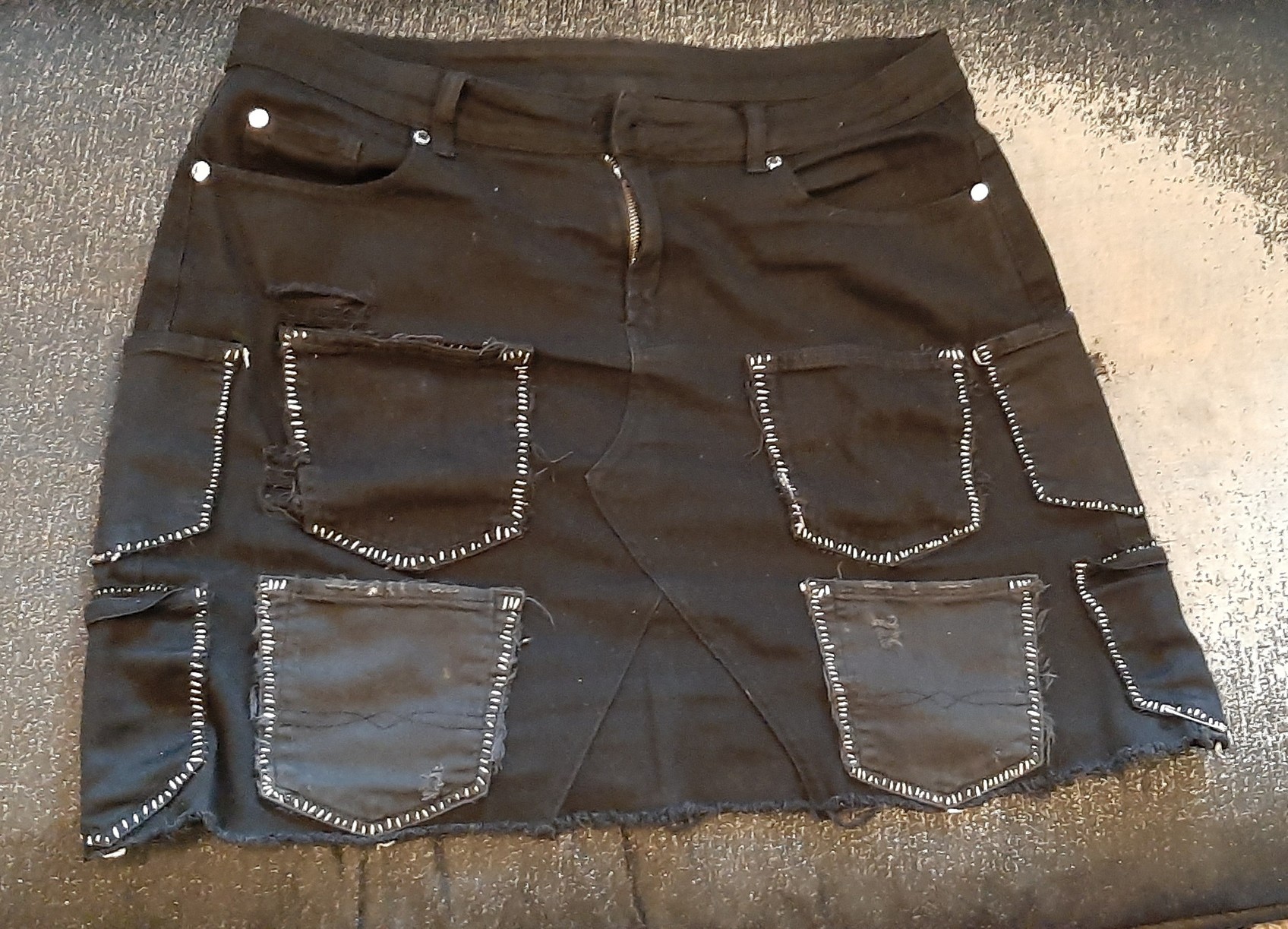 a black denim skirt with eight black demim pockets sewn onto the front with white waxed dental floss